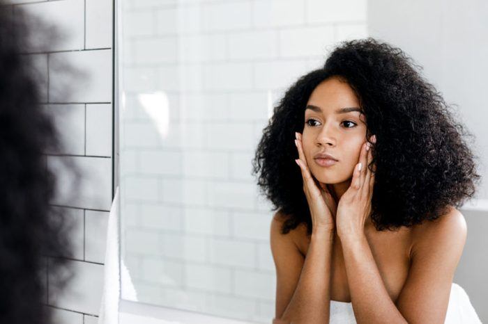 Woman massaging her face and looking at a mirror.