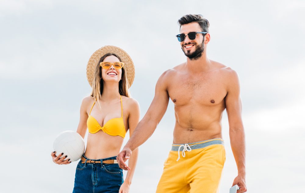 beautiful young couple in beach clothes with volleyball ball in front of cloudy sky
