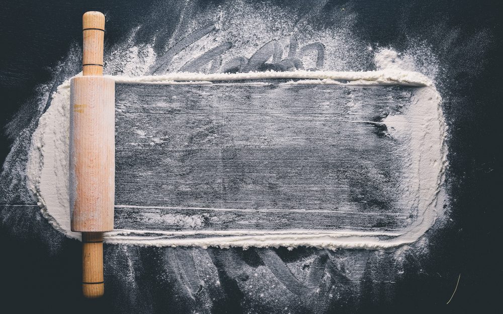 Rolling pin and white flour on a dark background. 