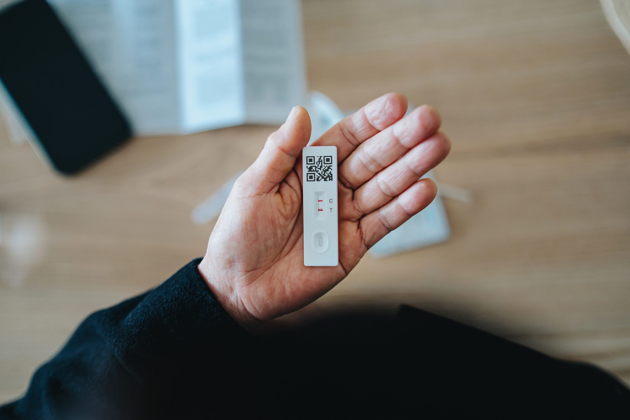 Overhead view of senior person carrying out a Covid-19 rapid lateral flow test at home. She is holding a positive Coronavirus rapid self test device, feeling worried