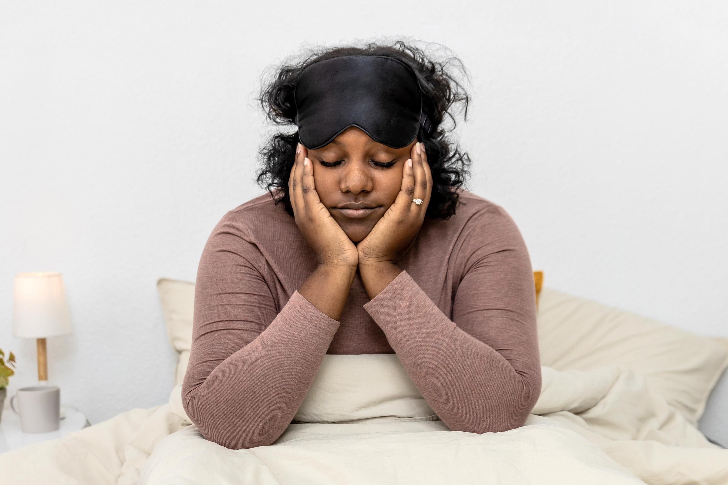 tired woman sitting in bed with an eye mask on her head