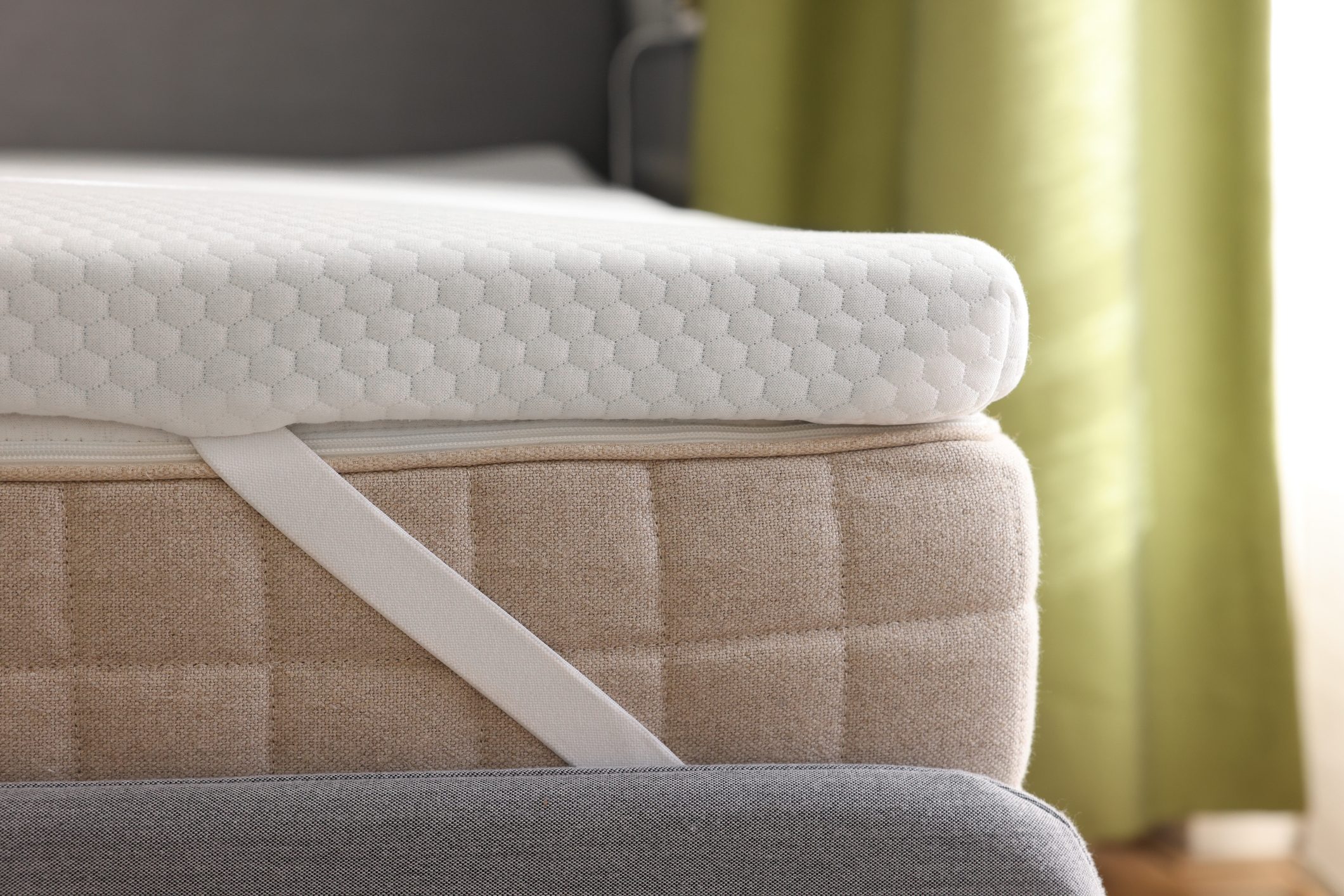 White memory foam mattress topper on grey bed, closeup