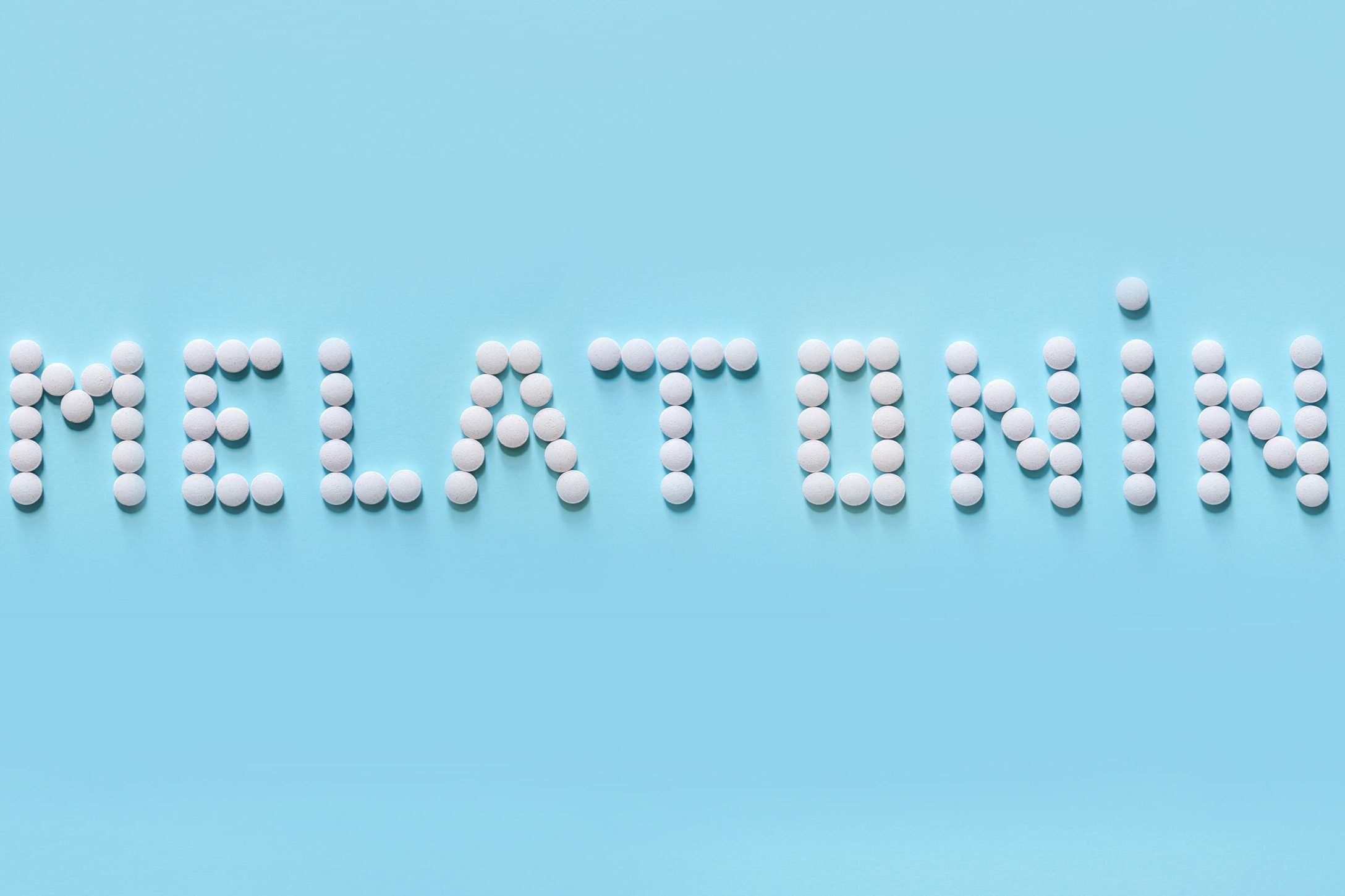 Melatonin, the word is laid out on a blue background of tablets. Tablets, hormone and excipients to improve sleep.
