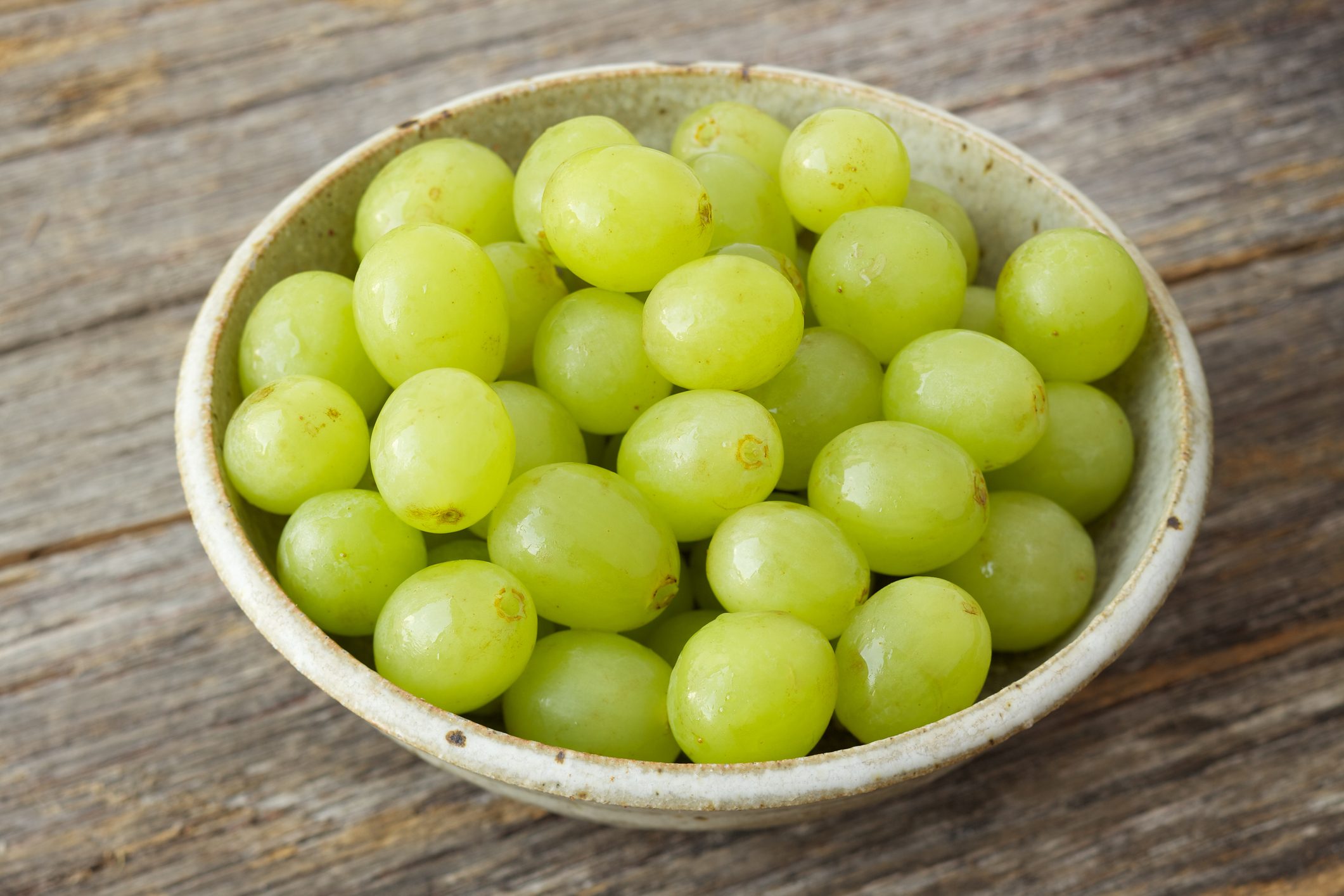Small bowl of organic green grapes on rustic wood