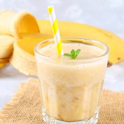 banana smoothie in a glass. whole and cut bananas in the background