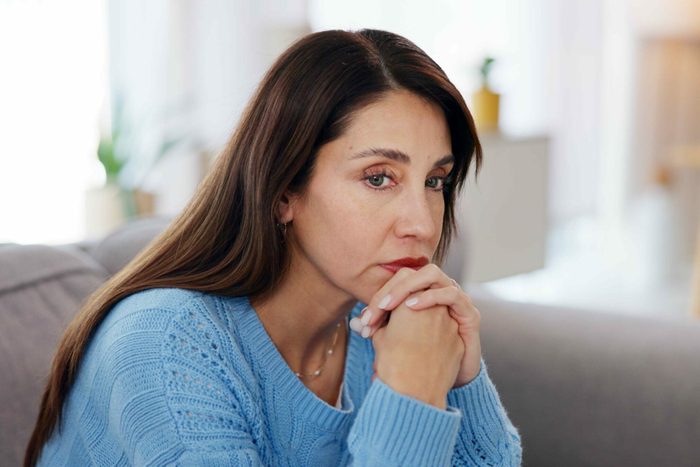 Woman, thinking and stress on sofa in home with financial crisis, jobless and overwhelmed with pressure. Person, thoughtful and worry on couch with depression, reflection and mortgage debt in lounge